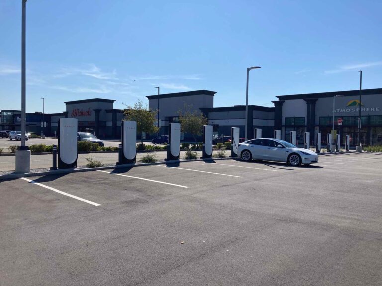 Un parking avec plusieurs bornes de superchargeurs V4 de Tesla, dont une est occupée par une voiture Tesla, à l'extérieur d'un centre commercial au Canada, marquant l'arrivée des superchargeurs V4 dans le pays.